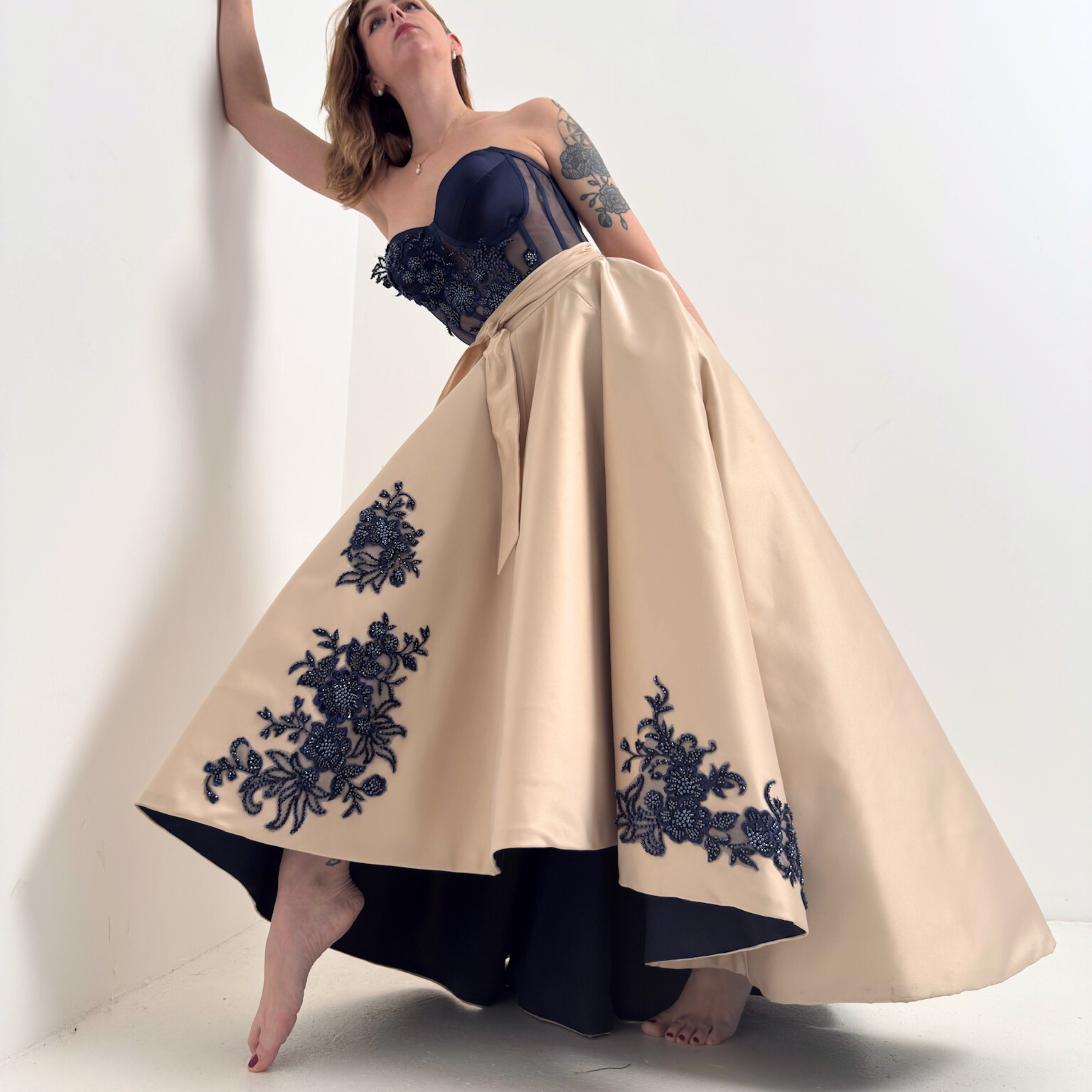 Model trägt asymmetrischen Tellerrock aus champagnerfarbenem Taft mit schwarzer Perlenstickerei von DEFONDO.