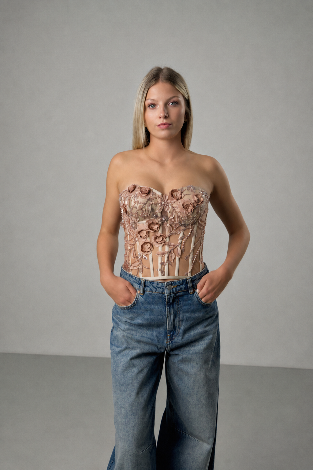 Floral besticktes Korsett mit zarten Blumenverzierungen, kombiniert mit einer blauen Jeans im minimalistischen Studio-Look.
